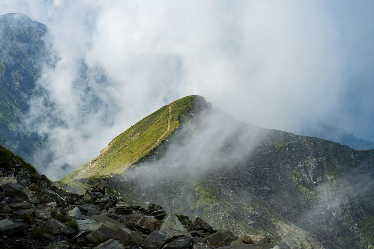 A thin hiking trail running up a green mountain ridge through drifting cloud.